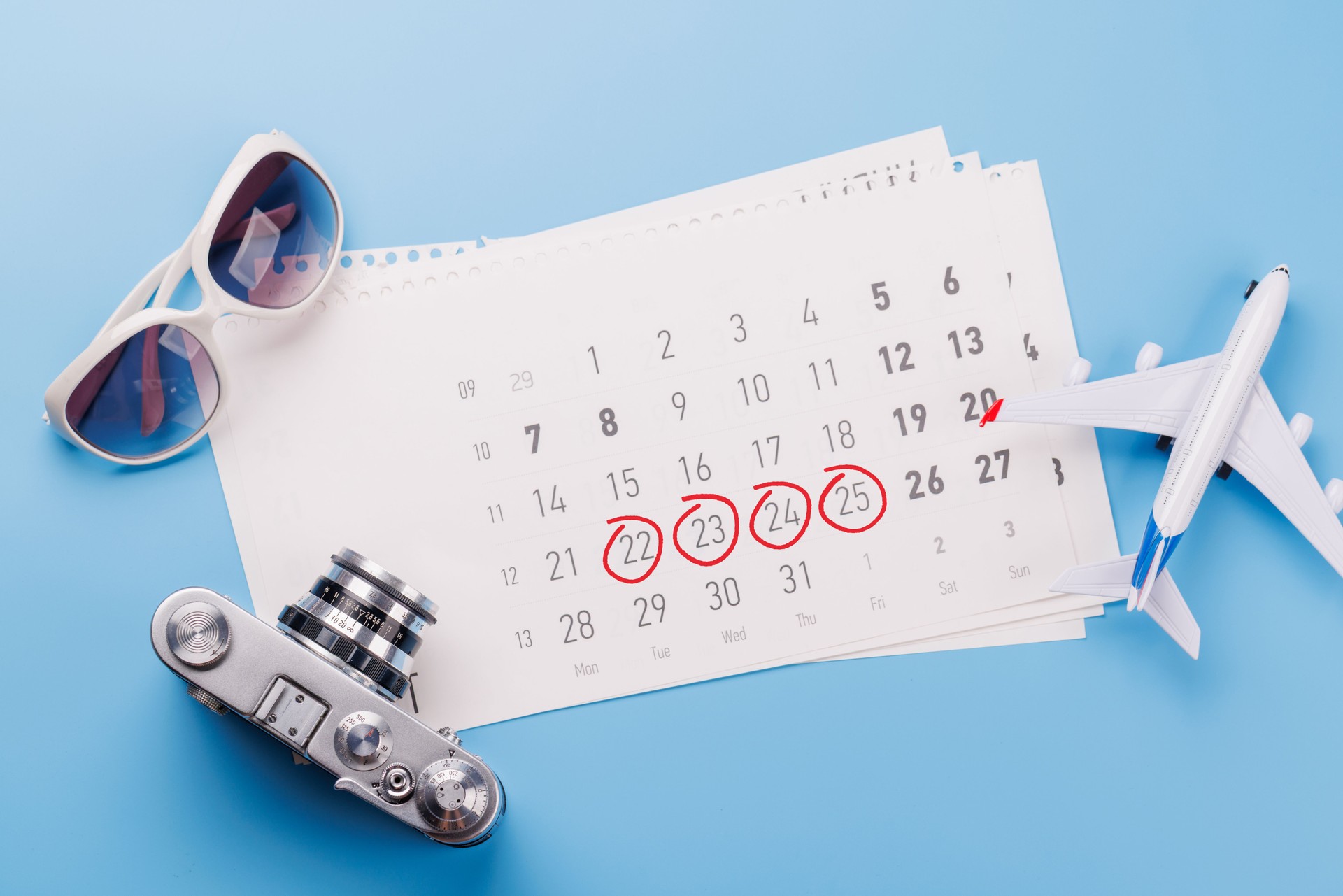 Travel-themed flat lay with calendar, toy airplane, camera, and sunglasses